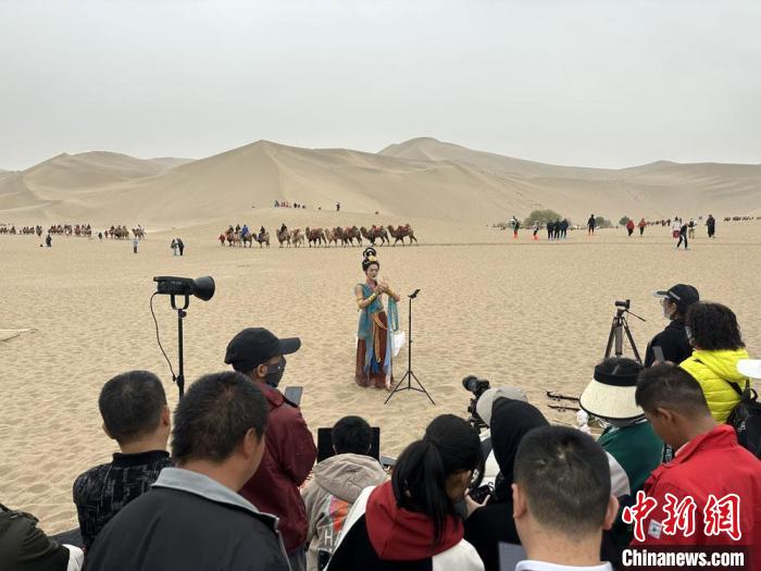 圖為2023年4月底，敦煌大漠“逐舞者”奧楠在鳴沙山月牙泉景區(qū)視頻直播，吸引游人圍觀。　馮志軍 攝